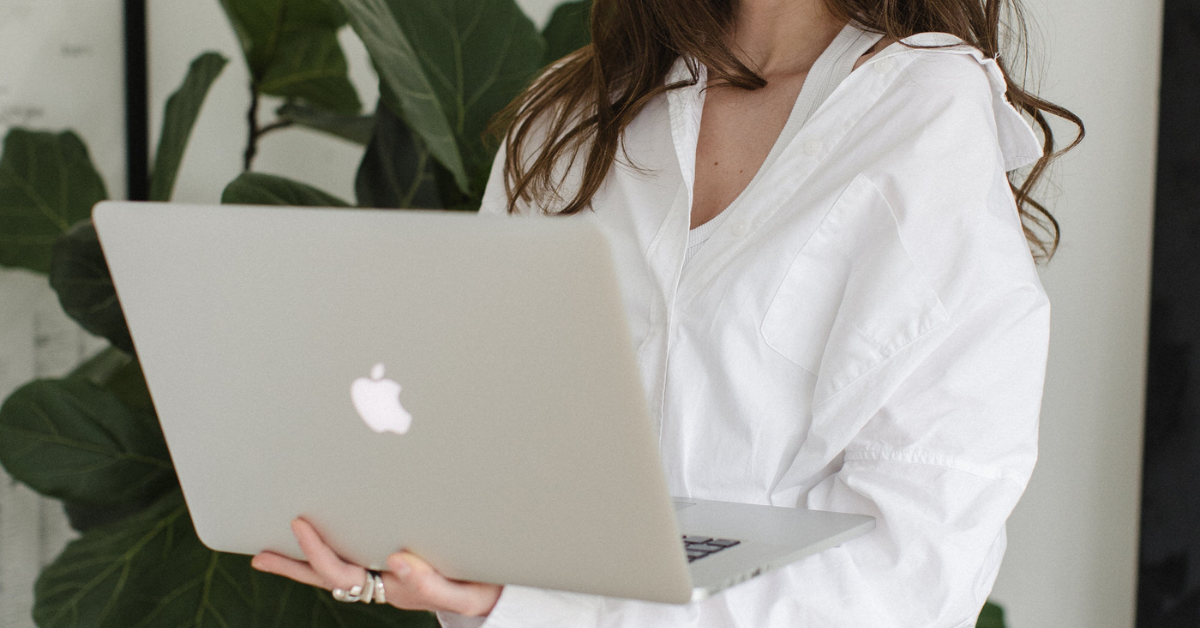 woman in white linen shirt typing on a Macbook