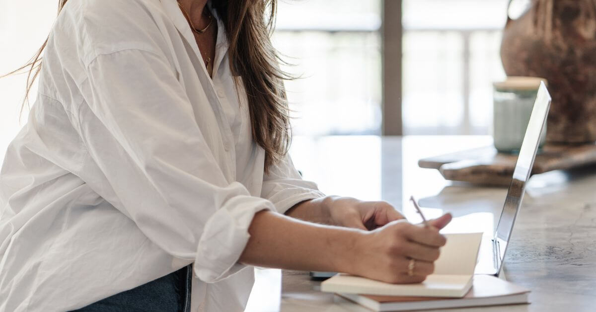 woman in white button-down shirt writing in notebook